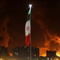 Banderas iraníes ondean mientras el fuego y el humo de un ataque israelí contra el depósito de petróleo de Sharan se elevan, tras los ataques israelíes contra Irán, en Teherán, Irán, el 15 de junio de 2025. 
