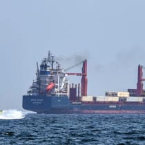 Una embarcación se aproxima al buque portacontenedores Marsa Victory, con bandera de San Cristóbal y Nieves, mientras navega por las aguas del estrecho de Ormuz, frente a la costa de Khasab, en la península de Musandam, al norte de Omán, el 25 de junio de 2025. 