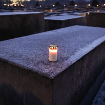 A single lit candle lies on a frost covered concrete block at the Memorial to the Murdered Jews of Europe on January 26, 2026 in Berlin, Germany.