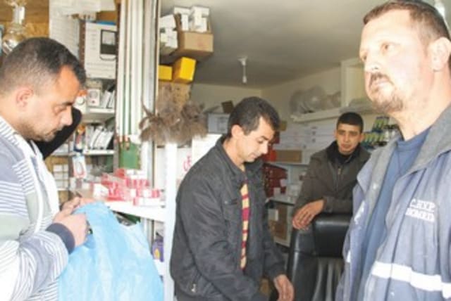 RELIGIOUS SETTLER Yanki Herchkov (right) shops last week in the store that Mustafa Sabateen (center) owns in the West Bank Palestinian village of Husan. (photo credit: TOVAH LAZAROFF)
