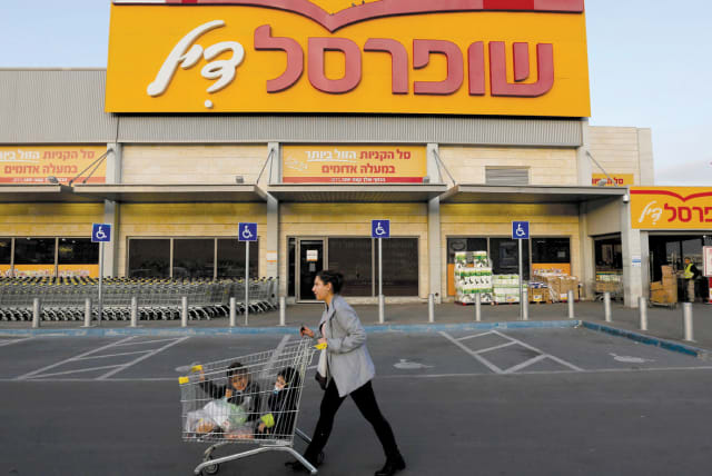 A WOMAN pushes children in a shopping cart in front of a Shufersal ‘Sheli’ in Ma’aleh Adumim (photo credit: AMMAR AWAD/REUTERS)