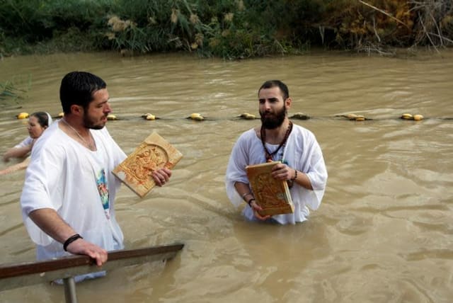 Christian pilgrims dip in the waters of the Jordan River during a baptism ceremony at the Qasr el-Yahud site, near Jericho, in January. (photo credit: MUSSA QAWASMA / REUTERS)