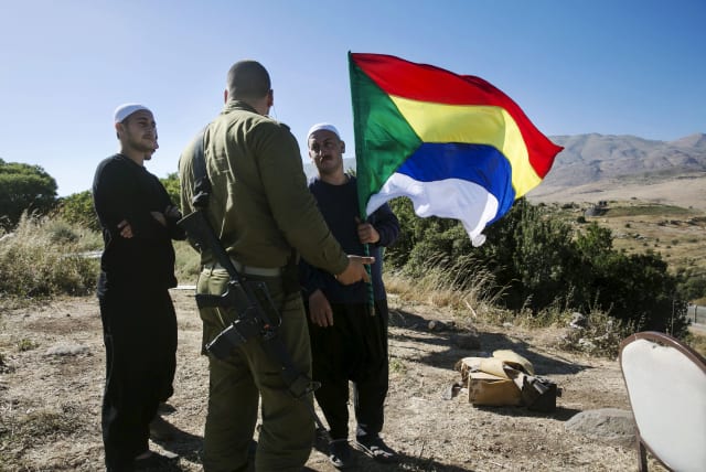 A member of the Druze community holds a Druze flag as he speaks to an Israeli soldier near the border fence between Syria and the Golan Heights, near Majdal Shams June 18, 2015. Gathered at a hilltop in the Golan Heights, a group of Druze sheikhs look through binoculars at the Syrian village of Hade (photo credit: BAZ RATNER/REUTERS)