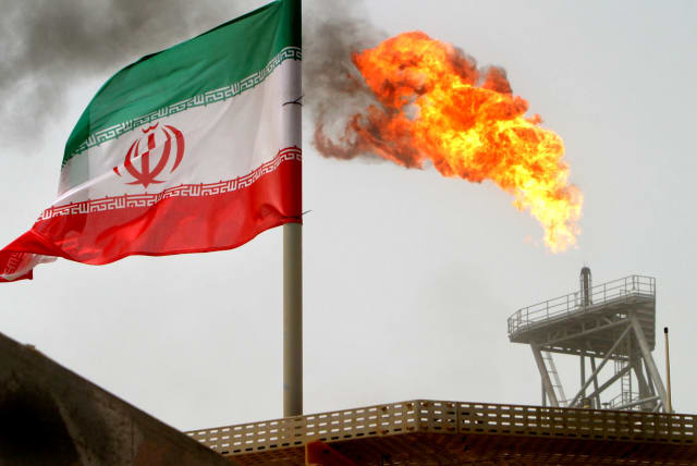 A gas flare on an oil production platform in the Soroush oil fields is seen alongside an Iranian flag in the Persian Gulf, Iran, July 25, 2005 (photo credit: RAHEB HOMAVANDI/REUTERS)
