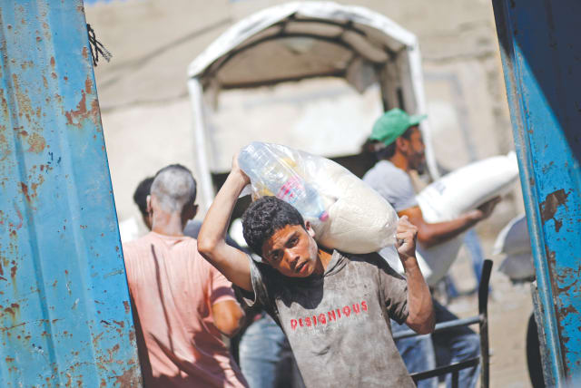 A PALESTINIAN carries food supplies at a Gaza aid distribution center run by the United Nations Relief and Works Agency (UNRWA), in the Al-Shati refugee camp (photo credit: MOHAMMED SALEM/REUTERS)