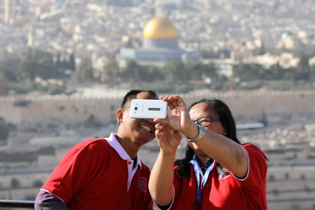 Tourists look at a mobile phone as they stand at an observation point overlooking the Dome of the Rock and Jerusalem's Old City (photo credit: REUTERS)