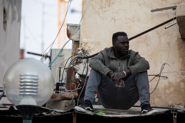 An African migrant sits near the Old Central Bus Station in south Tel Aviv, Israel February 3, 2020 (photo credit: REUTERS/AMIR COHEN)