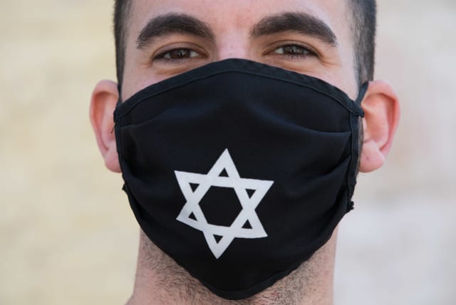 A man wears a face mask  with David Star at the Nachlaot Neighborhood in Jerusalem on April 12, 2020. A full closure on 17 Jerusalem Neighborhoods went into effect today at noon in efforts to contain the spread of the coronavirus. (photo credit: NATI SHOCHAT/FLASH 90)