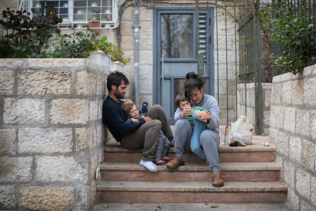 An Israeli family sits on the steps outside their apartment building in Jerusalem, as they stay at home with their children during a nation-wide quarantine, on March 31, 2020.  (photo credit: HADAS PARUSH/FLASH90)