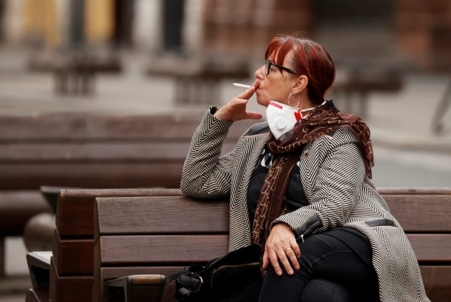 A woman smokes a cigarette as she sits on a bench in Liverpool, following the outbreak of the coronavirus disease (COVID-19), Liverpool, Britain, May 26, 2020 (photo credit: PHIL NOBLE/REUTERS)