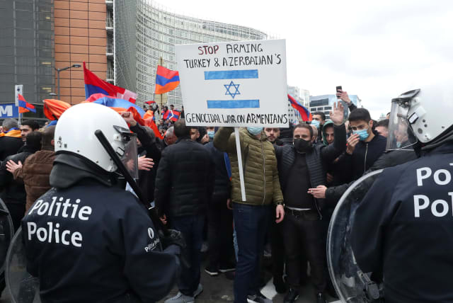 Demonstrators supporting Armenia hold a sign protesting Israel's sale of arms to Azerbaijan in the military conflict over the breakaway region of Nagorno-Karabakh, in Brussels, Belgium October 7, 2020 (photo credit: REUTERS/YVES HERMAN)