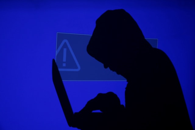 A hooded man holds a laptop computer as a blue screen with an exclamation mark is projected on him in this illustration picture taken on May 13, 2017.  (photo credit: REUTERS/KACPER PEMPEL/ILLUSTRATION/FILE PHOTO)