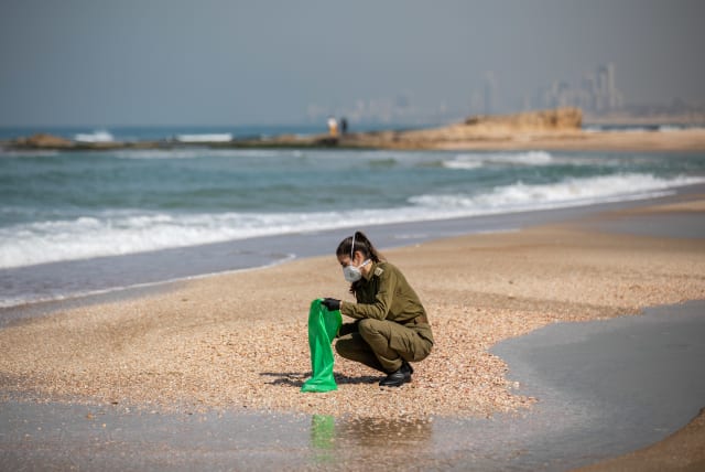 Israeli soldiers clean tar off the Palmachim beach following an offshore oil spill which drenched most of the Israeli coastline, February 22, 2021 (photo credit: YONATAN SINDEL/FLASH 90)