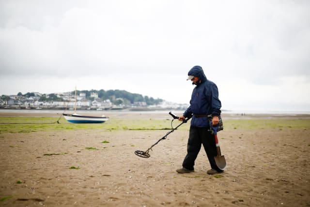 A man uses a metal detector on the beach. (photo credit: REUTERS/HENRY NICHOLLS)
