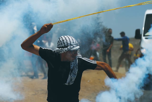   A PALESTINIAN DEMONSTRATOR uses a slingshot during a protest against settlements. (photo credit: MOHAMAD TOROKMAN/REUTERS)
