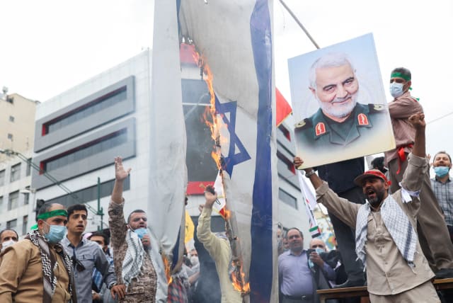 A man holds up a poster of the late Iranian Major-General Qassem Soleimani next to a burning Israeli flag as Iranians attend a rally marking the annual Quds Day, or Jerusalem Day, on the last Friday of the holy month of Ramadan in Tehran, Iran April 29, 2022 (photo credit: WANA NEWS AGENCY/REUTERS)