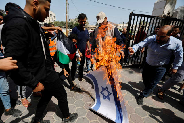  Palestinians burn a representation of an Israeli flag during a protest over tensions in Jerusalem's al-Aqsa Mosque, in Khan Younis, in the southern Gaza Strip, on Jerusalem Day, on May 29, 2022.  (photo credit: IBRAHEEM ABU MUSTAFA/REUTERS)