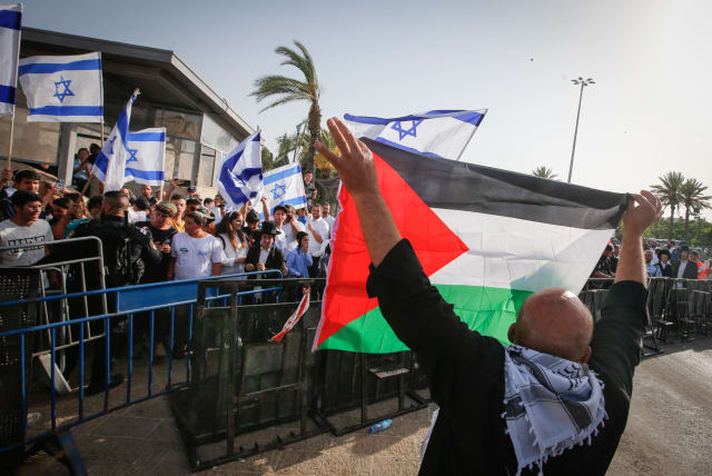 A man holds a Palestinian flag near young Jewish men holding Israeli flags in Jerusalem's Old City during Jerusalem Day celebrations, May 29, 2022. (photo credit: JAMAL AWAD/FLASH90)