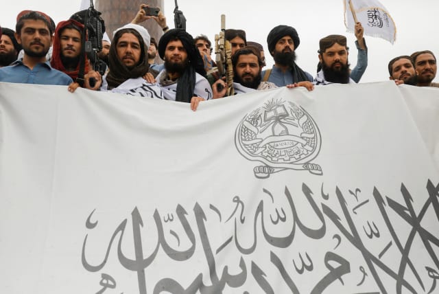  Taliban fighters hold an Islamic Emirate of Afghanistan flag on the first anniversary of the fall of Kabul on a street in Kabul, Afghanistan, August 15, 2022. (photo credit:  REUTERS/ALI KHARA)