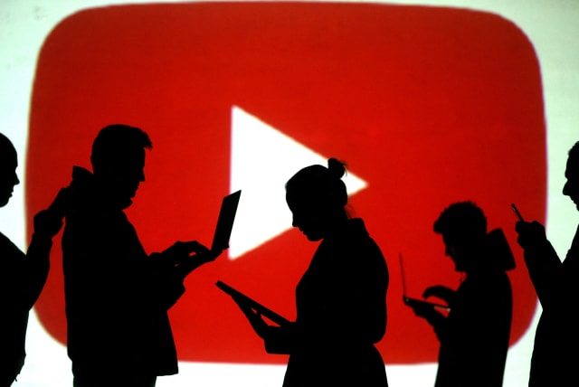   Silhouettes of laptop and mobile device users are seen next to a screen projection of the YouTube logo in this picture illustration taken March 28, 2018.  (photo credit: REUTERS/DADO RUVIC/ILLUSTRATION/FILE PHOTO)