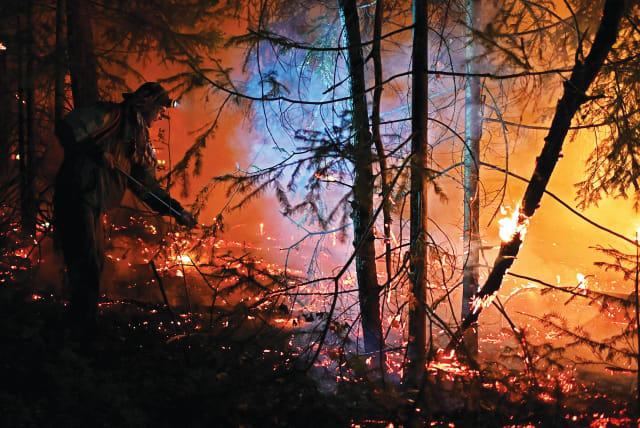  A VOLUNTEER WORKS to extinguish a wildfire raging on the federal highway in the Sverdlovsk region of Russia, last month. (photo credit: ALEXEY MALGAVKO/REUTERS)