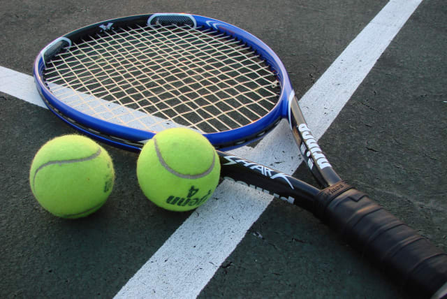 A tennis racket and two tennis balls on a court (photo credit: VLADSINGER/CC BY-SA 3.0 (http://creativecommons.org/licenses/by-sa/3.0/)/VIA WIKIMEDIA COMMONS)