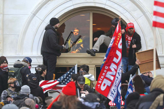  A MOB of supporters of then-US president Donald Trump climb through a window they broke, as they storm the United States Capitol Building in Washington, on January 6, 2021 (photo credit: LEAH MILLIS/REUTERS)