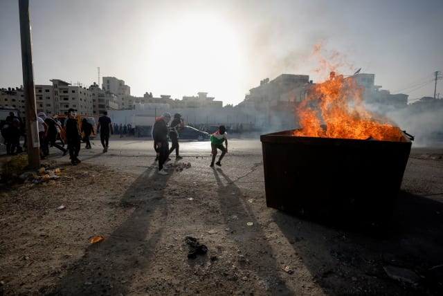 People are pictured next to a fire burning in a large container as Palestinians clash with Israeli forces during a protest over tensions in Jerusalem's Al-Aqsa Mosque on May 29, 2022 (photo credit: REUTERS/MOHAMAD TOROKMAN)