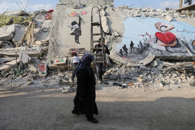  A woman walks past street art on the rubble of damaged buildings in the rebel-held town of Jandaris, in the aftermath of a deadly earthquake, in Syria February 22, 2023 (photo credit: REUTERS/KHALIL ASHAWI)