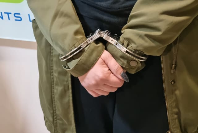  A suspect is seen in handcuffs, arrested after an Israel Police raid on a crime ring that defrauded tens of millions from Israel's National Insurance, on February 28, 2023. (photo credit: POLICE SPOKESPERSON'S UNIT)