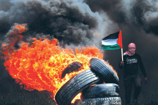  A MAN holds a Palestinian flag and tires are burned at the Israel-Gaza border fence, during a protest against the Israeli-Palestinian meeting in Sharm el-Sheikh, on Sunday. (photo credit: MOHAMMED SALEM/REUTERS)