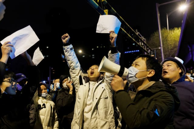 People shout slogans and hold up papers during a protest against coronavirus disease (COVID-19) restrictions after a vigil for the victims of a fire in Urumqi, as outbreaks of COVID-19 continue, in Beijing, China, November 28, 2022. (photo credit: THOMAS PETER/REUTERS)