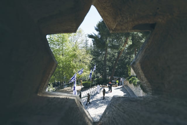  ISRAELI FLAGS and people are seen through a Star of David-shaped hole in a wall at Jerusalem’s Mount Herzl military cemetery on Remembrance Day.  (photo credit: RONEN ZVULUN/REUTERS)