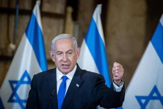 Israeli Prime Minister Benjamin Netanyahu, standing in front of Israeli flags, leads the weekly government conference, held at the Western Wall tunnels in Jerusalem's Old City on May 21, 2023. (photo credit: YONATAN SINDEL/FLASH90)