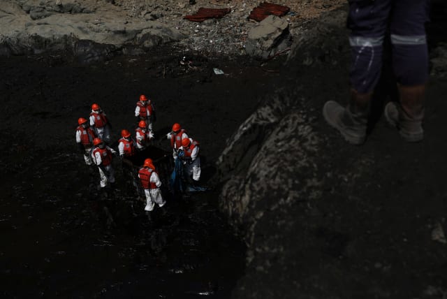 Workers clean up an oil spill following an underwater volcanic eruption in Tonga, in Ventanilla, Peru January 25, 2022. (photo credit: REUTERS/PILAR OLIVARES)