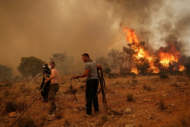  Men help a firefighter as they try to extinguish a wildfire burning near the village Vlyhada, near Athens, Greece, July 19, 2023. (photo credit: REUTERS/STELIOS MISINAS)