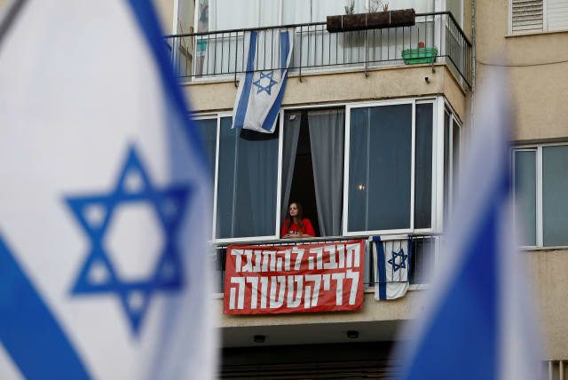  A person looks out, above a banner that reads 'in it to oppose the dictatorship', as people take part in a demonstration against Israeli Prime Minister Benjamin Netanyahu and his nationalist coalition government's judicial overhaul, in Tel Aviv, Israel, July 22, 2023. (photo credit: CORINNA KERN/REUTERS)