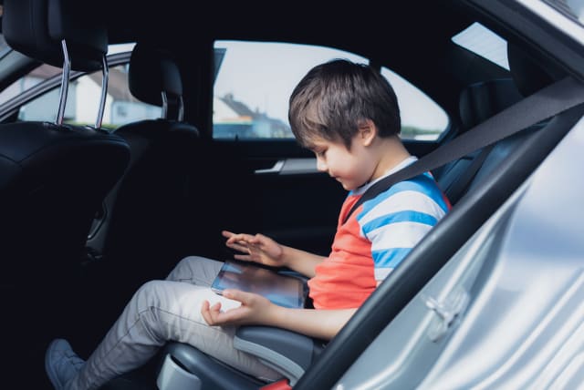 A young child uses a tablet in the back seat of a car (illustrative) (photo credit: INGIMAGE)