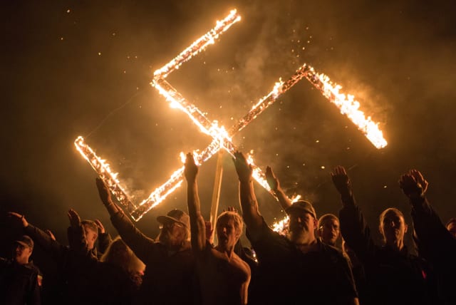 Supporters of the National Socialist Movement, a white nationalist political group, give Nazi salutes while taking part in a swastika burning at an undisclosed location in Georgia, U.S. on April 21, 2018.  (photo credit: REUTERS)