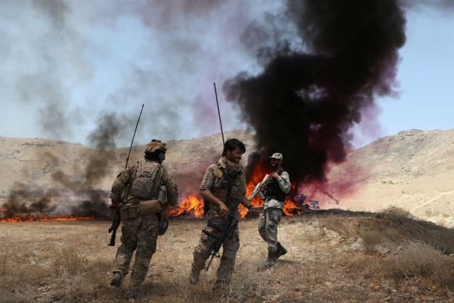  Afghan police officers chat with each others in front of a pile of burning illegal drugs in the outskirts of Kabul, Afghanistan July 1, 2021. (photo credit: REUTERS/OMAR SOBHANI)