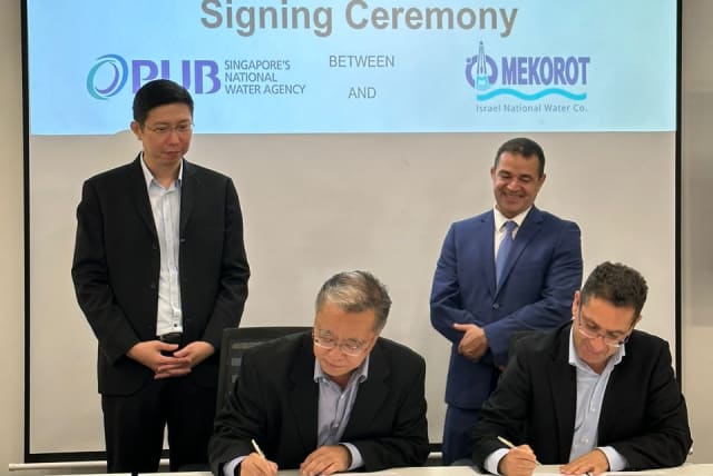  Mekorot vice-president of engineering Yossi Yaakobi signs MOU with PUB assistant CEO, as Mekorot CEO Amit Lang (standing at right) looks on. (photo credit: MEKOROT)