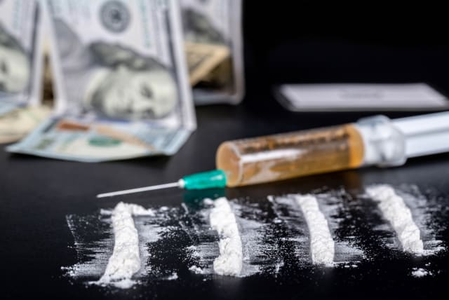  White powder sprinkled on a black background, behind money and a syringe with drugs. (photo credit: FLICKR)