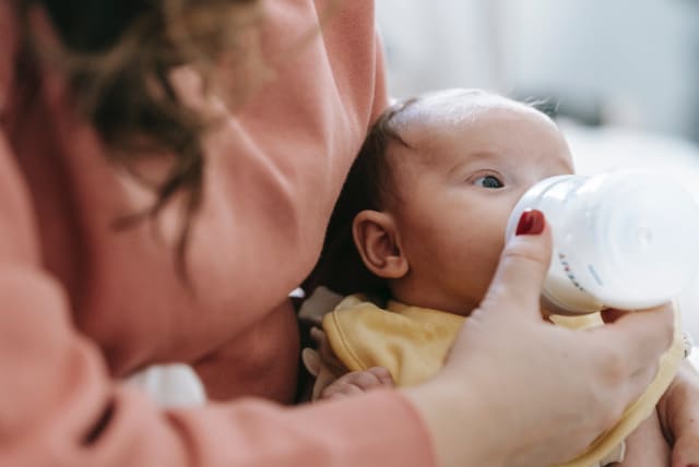  A holds a baby and feeds them milk from a bottle. (photo credit: PEXELS)