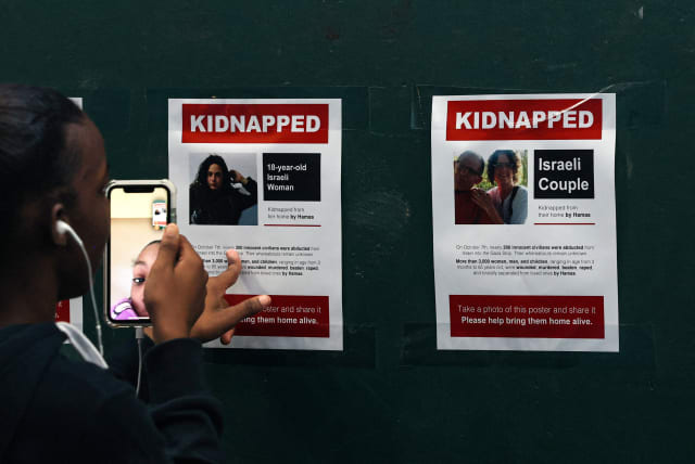 A girl records video of flyers in Times Square, of Israeli people reported missing as the city reacts to the ongoing conflict between Israel and the Palestinian terrorist group Hamas, in New York City, US, October 12, 2023. (photo credit: BRENDAN MCDERMID/REUTERS)