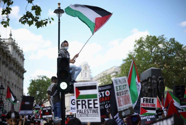  A protester holds a flag as he sits on a traffic light post during a (different, years earlier) pro-Palestine demonstration outside Downing Street in London, Britain, June 12, 2021. (photo credit: REUTERS/HENRY NICHOLLS)
