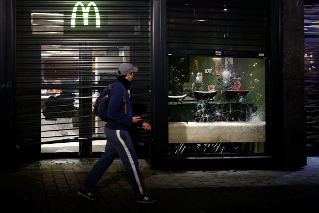 A man walks by while looking at a vandalized McDonald's as demonstrators gather in Nantes to protest after French Prime Minister Elisabeth Borne used the article 49.3, a special clause in the French Constitution, to push the pensions reform bill through the National Assembly without a vote by lawmak (photo credit: REUTERS/STEPHANE MAHE)