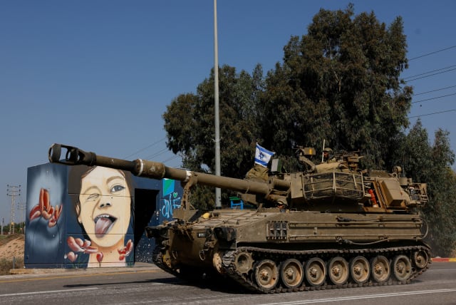  View of a mural as Israeli soldiers from an artillery unit ride a military vehicle near the Israeli side of the border between Israel and the Gaza Strip, November 3, 2023 (photo credit: REUTERS/AMIR COHEN)