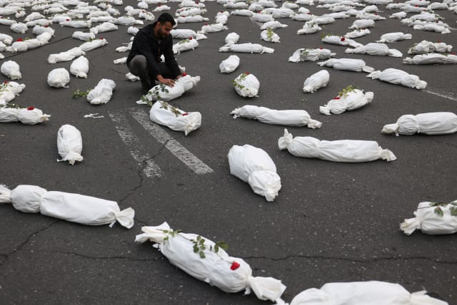 An Iranian man sits next to the symbolic shrouds of Gaza children's dead bodies during a gesture in a street in Tehran, Iran November 13, 2023. (photo credit: MAJID ASGARIPOUR/WANA/REUTERS)