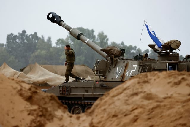An Israeli soldier walks near a mobile artillery unit near the northern Gaza border, in southern Israel, November 19, 2023 (photo credit: REUTERS/AMIR COHEN)