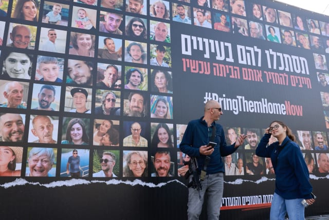 People walk next to pictures of civilians held hostage by Hamas terrorists in Gaza, in Jerusalem, November 22, 2023 (photo credit: MARC ISRAEL SELLEM/THE JERUSALEM POST)